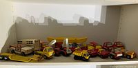 Wide view showing entire collection of toy Tonka trucks and a yellow canoe, displayed on a white shelf.