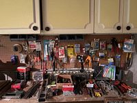 Wide view of assorted hand tools and hardware on pegboard and table surface