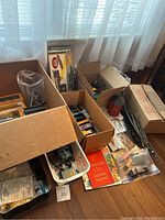 Wide shot showing several boxes and a basket containing various HO scale train cars and accessories, including original packaging and paper materials.