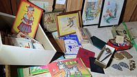 Box containing vintage greeting cards, postcards, various illustrated cards, Little Zebra coloring book, and other paper ephemera alongside footwear, charm bracelet, and collectibles.