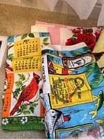 Photo displaying folded vintage linen hand towels with printed calendar and cocktail motifs, showing bright colors with bird and nautical themes.