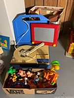 Overall view of Etch A Sketch, record player, and box of figurines showing assortment of items included in lot