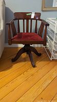 Full front view of oak captain’s chair showing wooden frame, spindles and red seat