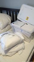 Single size bedding including cotton sheets, mattress covers, stacked on a bed with clear plastic tote for storage.