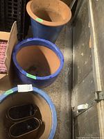 Top view and partial side view of three flower pots: two blue ceramic pots with terracotta interiors and one taller blue ceramic pot with a terracotta rim.
