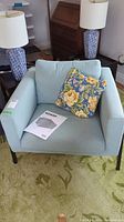 Light blue Ikea Koarp armchair with floral pillow on the seat and instruction manual placed on cushion, showing front view and design.