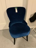 Front view of the deep blue velvet occasional chair showing the rounded backrest with button tufting and black legs.