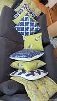Cushions arranged on a dark grey couch, showing the variety of patterns and colors including bird prints and blue geometric designs.