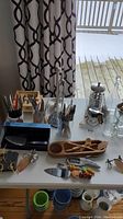 Overview of spreaders, cutters, bottle opener, wooden chip and dip bowl, glass decanter, and various metal utensils and cutlery.