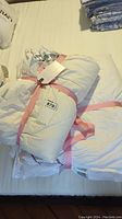 Two white twin sized duvets laid on a bed, wrapped with pink ribbons and tags attached.