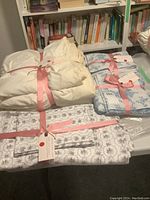 Two sets of Cabbage and Roses London queen duvet covers each bundled with three matching pillowcases tied with pink ribbons, on a table with books behind.