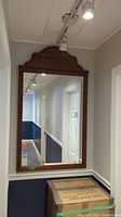 Full view of large rectangular wall mirror mounted on wall above boxes in hallway, showing wood frame and reflective glass surface.