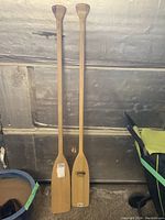 Two solid wood canoe paddles standing upright, showing full length and T-grips