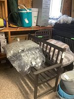 Wooden slat bench with cushions placed on it; cushions are white and dark patterned.