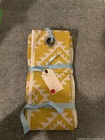 Folded yellow and white geometric patterned curtain panels with metal grommets tied with blue ribbons, lying on carpeted floor