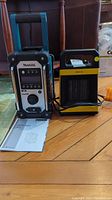 Makita Job Site Radio with user manual and small yellow and black room heater side by side on wood floor.