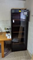 Full view of upright black wine cellar fridge with glass door showing wood shelves
