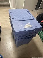 Three stacked large blue plastic storage bins with lids visible, placed on a wooden floor.
