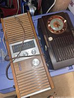 Two vintage radios placed on a blue plastic storage bin. One is dark brown with clock face and knobs, the other is a Viking brand radio with wooden panels and silver front showing tuning scale and knobs.