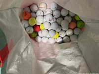 Overhead view inside a bag filled with golf balls of different brands and colors, mostly white, some orange, yellow, and green.