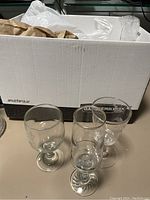 Photo of three stemmed glasses placed in front of a white Banker’s Box partially filled with additional glassware visible inside.