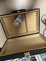 Open black cassette tape case with beige slots and one Sony cassette tape inside