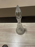 Clear crystal decanter with stopper standing on wood floor.