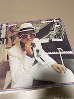 Photo showing the album cover of Elton John Greatest Hits vinyl record featuring Elton John in white suit by a piano.