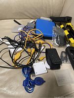 Photo showing various cables and accessories on a beige surface, featuring Game Boy-related white link cable adapter and other electronic wires and pouches