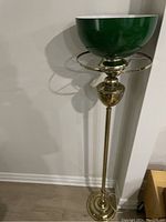 Tall floor lamp with green glass bowl shade and brass stand against white wall on hardwood floor.