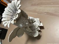 Top angled view of white angel cherub lawn ornament holding a large sunflower, with smaller flowers at base.