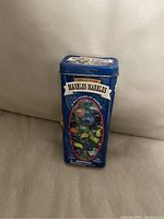 Blue rectangular tin container with a clear window showing colorful glass marbles inside. Tin is labeled with 'Marbles Marbles Kids Collection'.