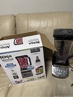 Photo showing Ninja Professional Blender 60oz in black and stainless with clear pitcher next to its original box on a beige couch.