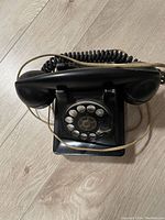 Front view of black rotary dial telephone with cords on wooden floor