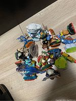 Photo showing 13 assorted Skylanders figures lying on a wooden surface, featuring multiple characters in various colors and sizes