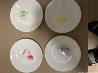Photo showing four small white plates each with a colored Mickey Mouse design in green, yellow, red, and blue.
