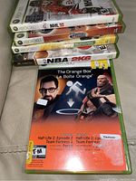 Photo shows a stack of five Xbox 360 game cases: NHL 10, Virtua Tennis, Scene It? Movie Night, NBA 2K6, and The Orange Box featuring Half-Life 2 and Team Fortress 2.