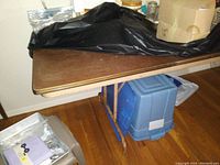 Photo shows close-up of the banquet table top and folding metal legs, alongside storage containers underneath the table.