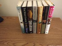 Image of eight hardcover books by John Grisham and Lynn Harris aligned side-by-side on wood surface, titles visible on spines.