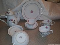 Full view of Royal Rose tea set pieces including teapot, cups, saucers, and plates, showing rose floral design and silver trim.