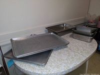 Two large metal pans placed on a patterned countertop, arranged stacked and slightly askew, showing surface texture and edges.