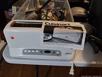 White Cuisinart wide slot toaster with control buttons and user manual sitting on a surface with other items in the background.