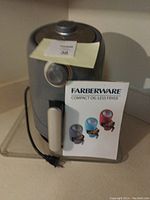 Gray Farberware compact oil-less air fryer with dial timer, handle, and power cord visible, accompanied by original instruction manual showing product in multiple colors.
