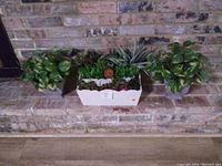 Three separate boxes containing artificial green and succulent plants positioned on stone steps outside.