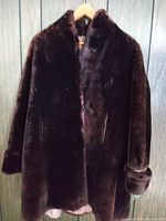 Full front view of a dark brown fur coat hanging on a wooden hanger against a wood-patterned backdrop.
