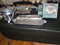 Photo showing multiple silver-plated serving dishes and platters on a table covered with black cloth.