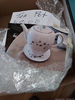 Photo of the teapot on its saucer wrapped in bubble wrap, with handwritten price tag visible