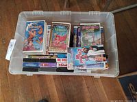 Plastic storage bin containing a collection of used VHS movies including Disney titles Hercules, The Little Mermaid, Dr. Dolittle, Superman, and The Secret of NIMH. VHS cases show typical wear from use.