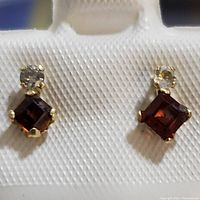 Close-up photo of the pair of garnet and diamond earrings displayed on white textured background