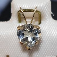 Close-up of heart-shaped aquamarine gemstone set in four prongs with a gold bail.